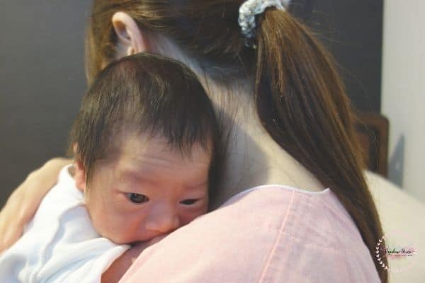 Mom is trying to burp the baby by patting and holding upright. 